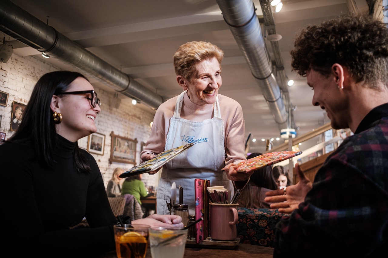 Senior-Mitarbeiterin Frau Marianne serviert im Generationencafé Vollpension in Wien