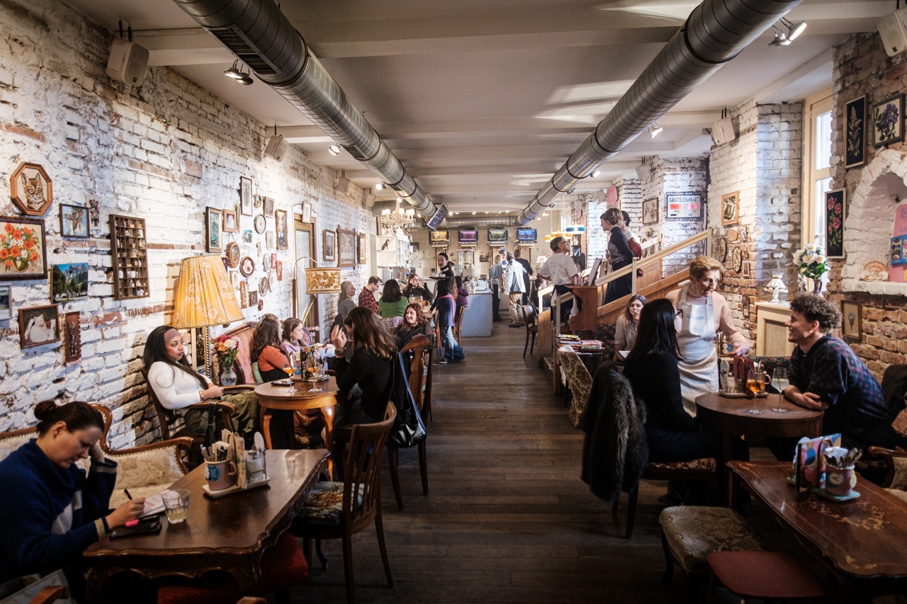 Gäste genießen Kuchen und Kaffee in Omas öffentlichem Wohnzimmer in der Vollpension Schleifmühlgasse